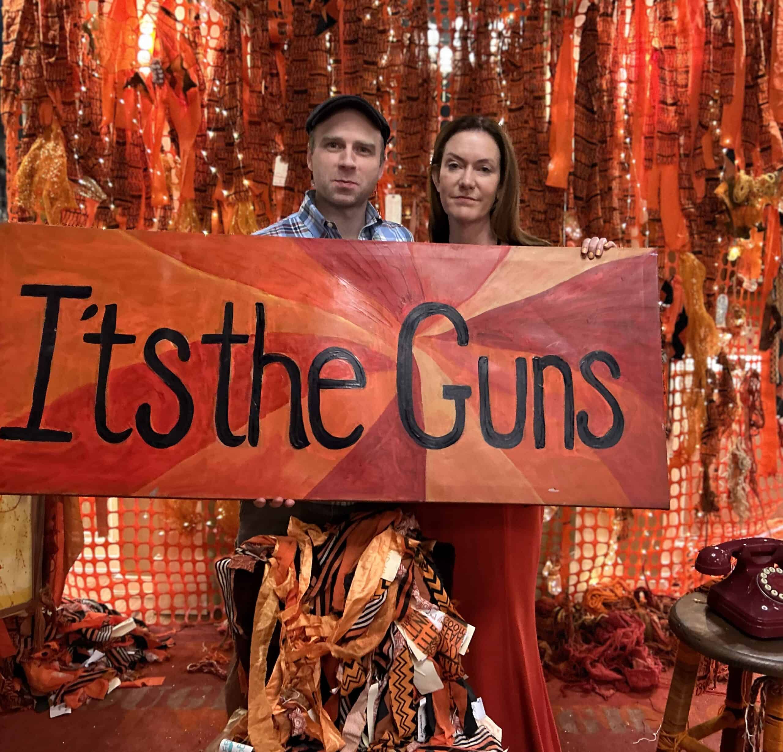 Selfie Photo Station. Two attendees hold a sign that reads: It's the Guns